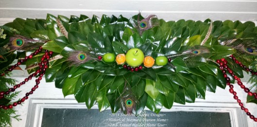 Fresh Magnolia-Leaf Crescent with Christmas Design Accents of Fresh Fruits & Feathers. Individual Cranberries and strung cranberries compliment a center assortment of a large green apple, two green limes and two fresh orange-peel roses. Peacock & pheasant feather accents were added for additional color & flair.