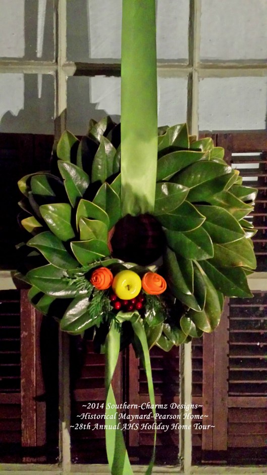 Close-up of our delicate, but charming fresh magnolia leaf wreath welcomes passers-by with a happy collection of Holiday fruits and foliage. Made of layers of fresh magnolia leaves, this traditional wreath is accented with fresh fruits: a green apple and two fresh orange peels fashioned into roses on either side nestled on a bed of cedar sprigs and a grouping of fresh cranberries. The trio of fruits represent the Holy Family and/or the Trinity as we festively look to celebrate the true spirit of Christmas.